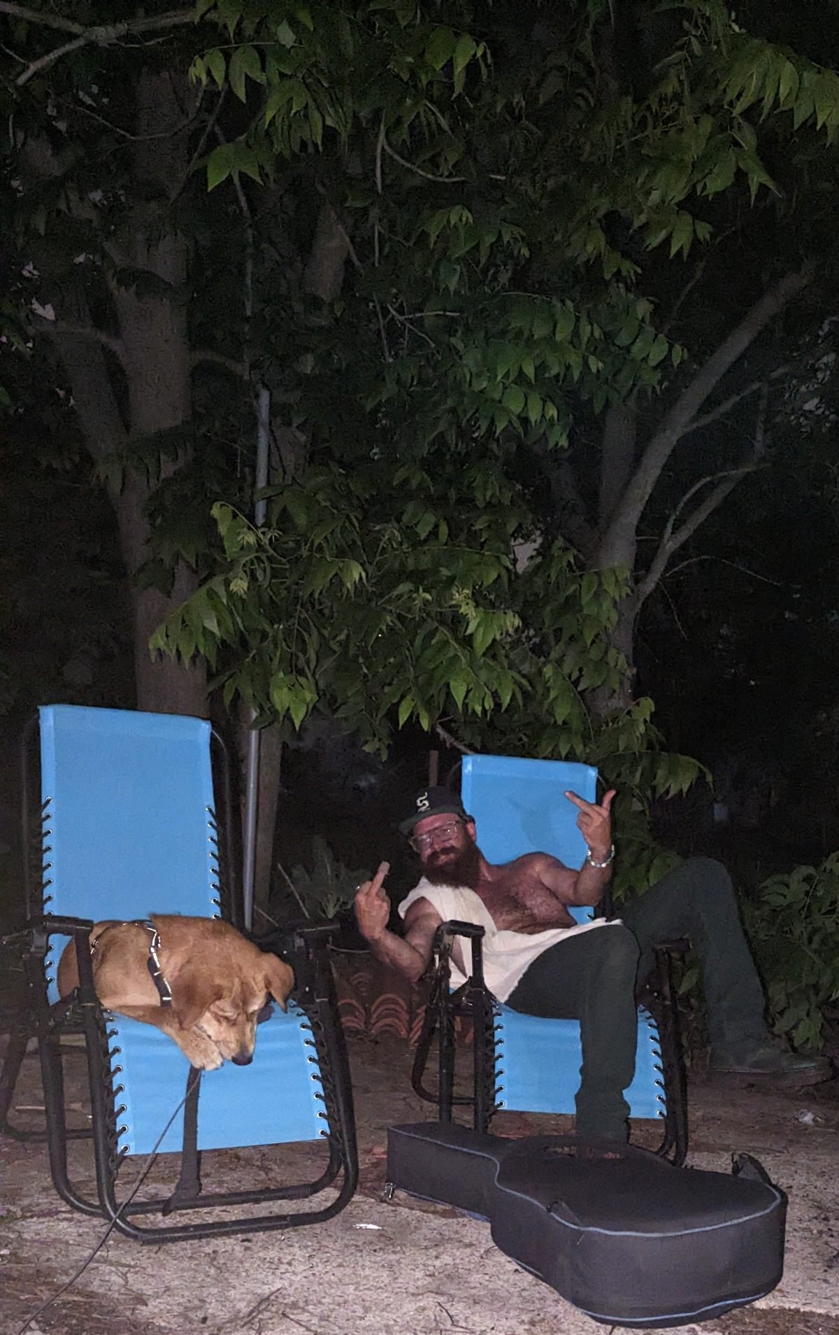 Deebo asleep in a lawn chair next to his human throwing up both middle fingers